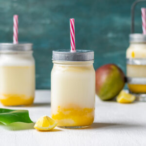 Blended, creamy mango lemonade in a jar with a lid and red straw.