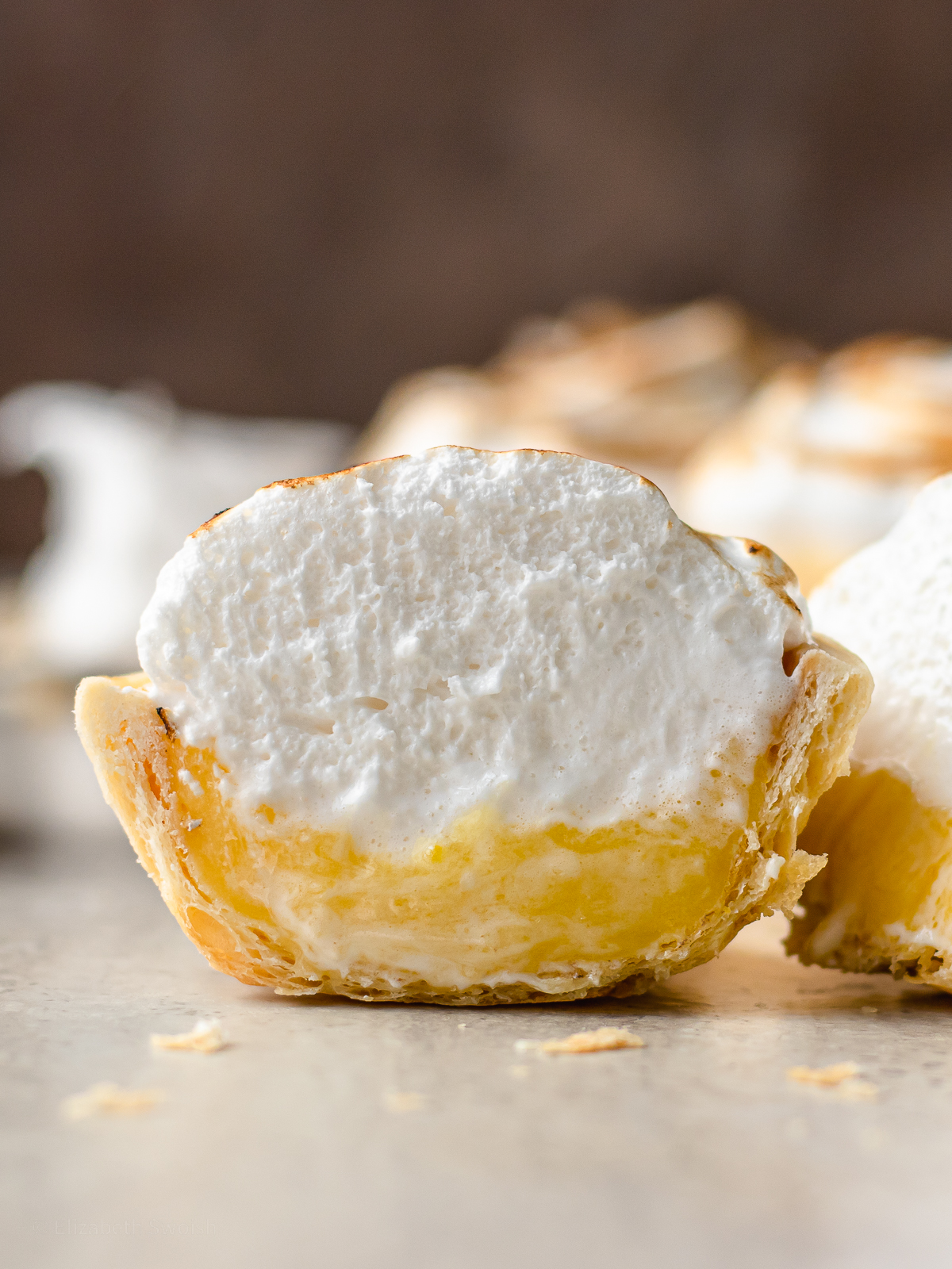 Mini Lemon Meringue Pie cut in half to see lemon curd, meringue, and a flaky pie shell.