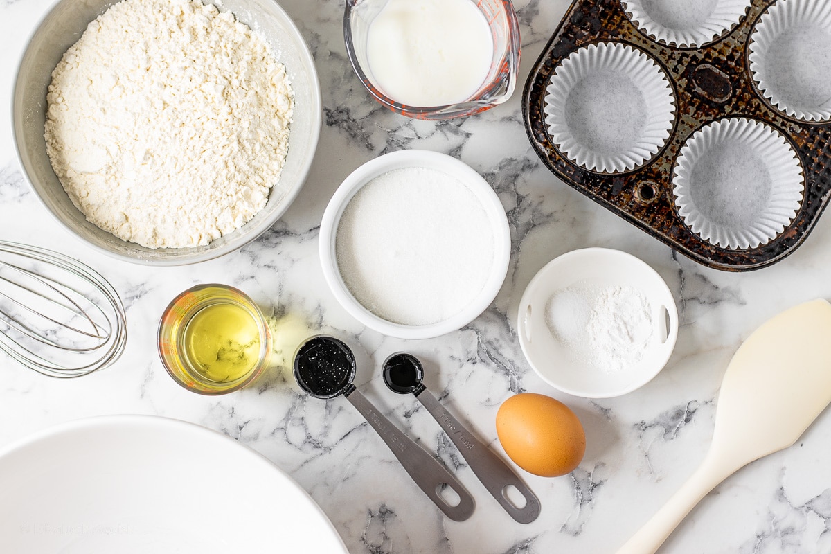 Ingredients for Coconut Cupcakes- Flour, Milk, Sugar, Baking Powder, Salt, Canola Oil, Egg. Whisk, Spatula, Prepared Cupcake Tin, and a Large Bowl for mixing and baking.