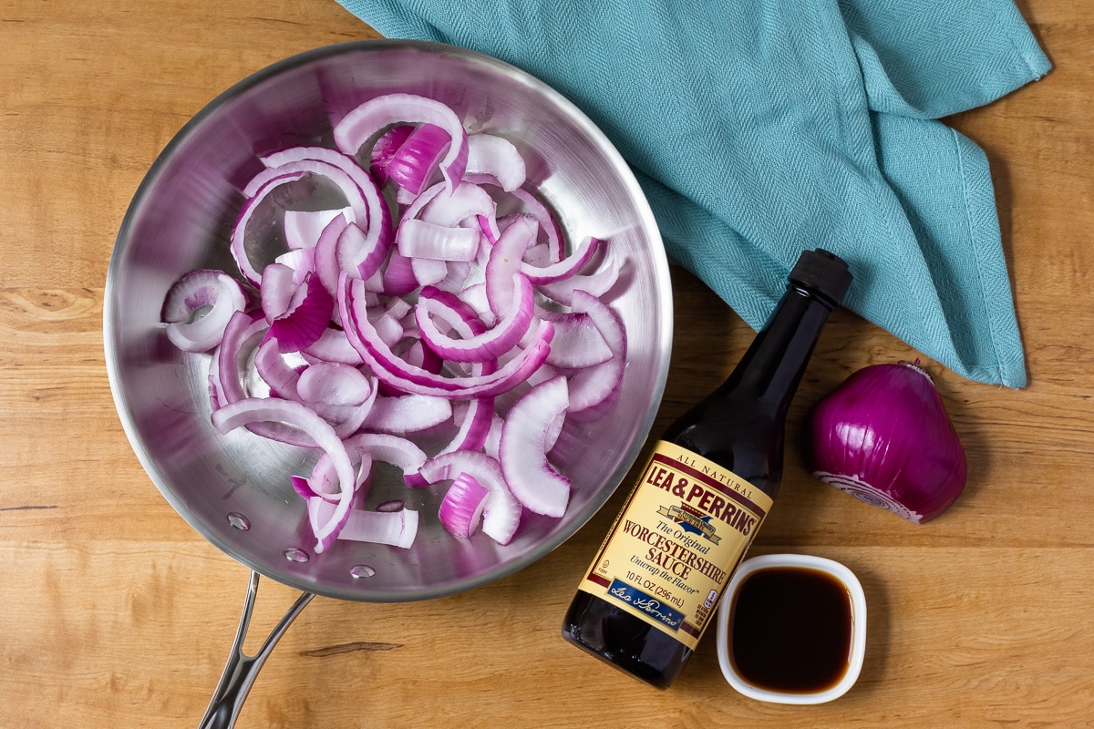 Caramelized Red Onion Ingredients- red onion in half slices and Worcestershire sauce. Stainless steel skillet for cooking.