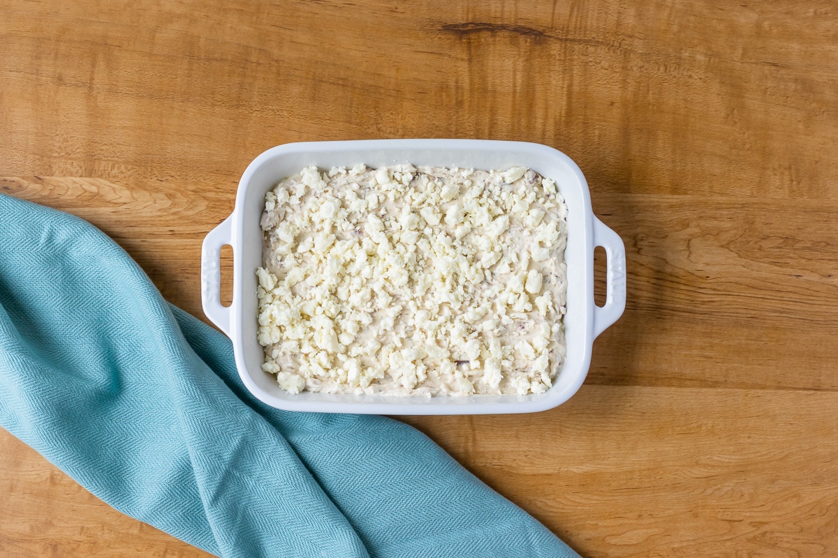 Feta & Onion Hot Dip in baking dish after red onion was blended into it. Dip is topped with left over feta cheese and is ready to go in the oven.