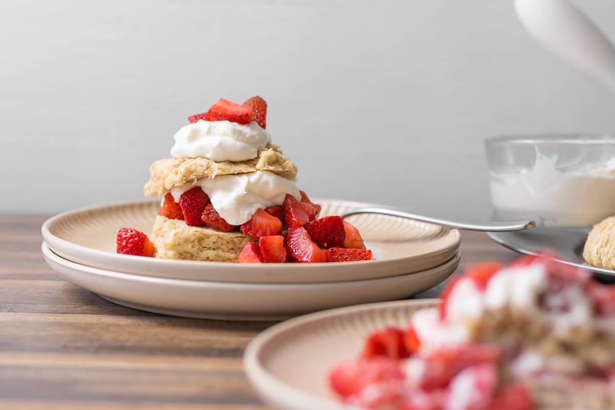 Strawberry Banana Shortcakes assembled and sitting on a decorative plate. Layers of shortcake, fresh strawberry syrup, and whipped cream. background focus