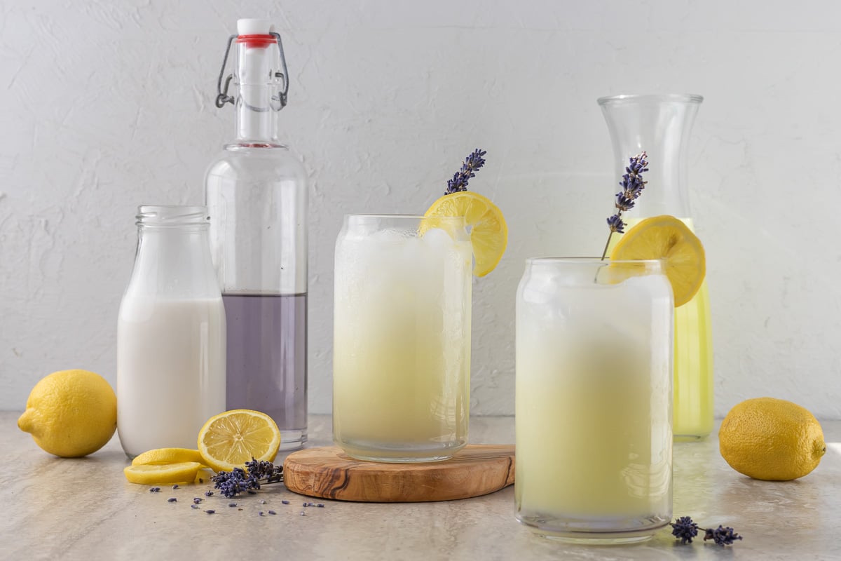 Lavender Coconut Lemonade. In background is Coconut Milk, Lavender Simple Syrup, and Lemonade as well as decorations of lemons and fresh lavender.