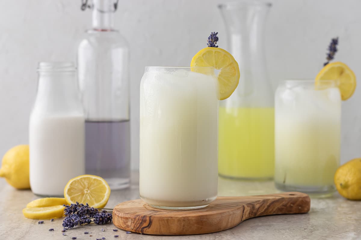 Lavender Coconut Lemonade Stirred Together. In background is Coconut Milk, Lavender Simple Syrup, and Lemonade as well as decorations of lemons and fresh lavender.