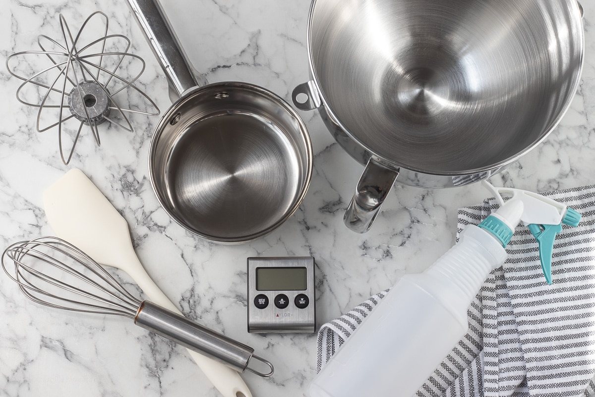 Overhead shot of tools needed for No Fail Italian Meringue including wire whisk, stand mixer and bowl, stainless steel pot, spatula, digital thermometer, vinegar and towel for cleaning the tools.