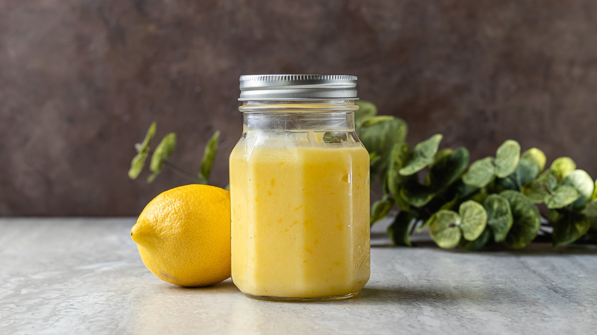Picture of lemon curd in a glass jar with a whole lemon next to it.