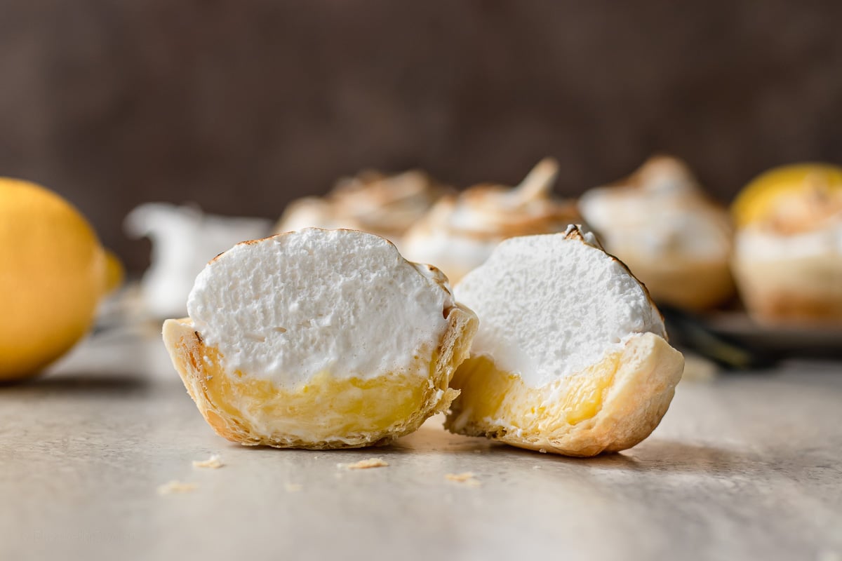 Slice shot of mini lemon meringue pies to see layers of crust, curd, and meringue.