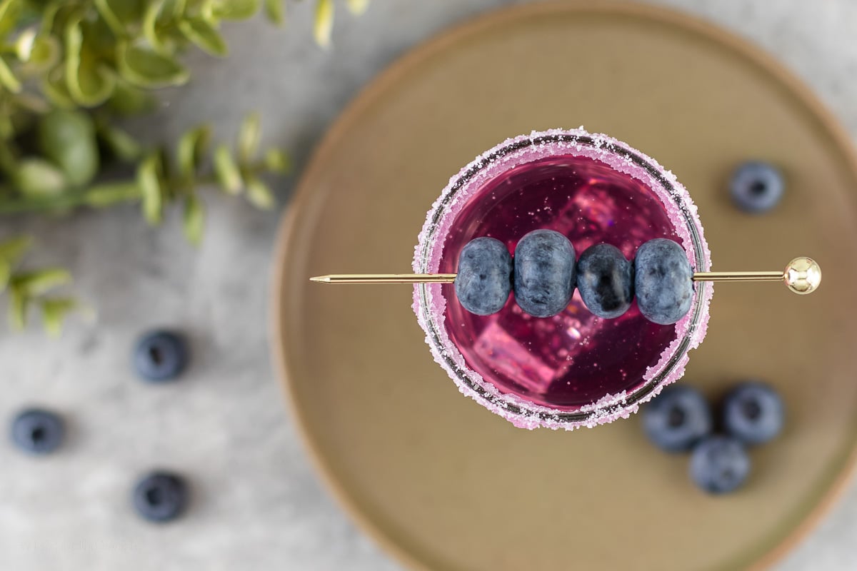 Overhead image of cocktail with blueberries on a gold cocktail pin.
