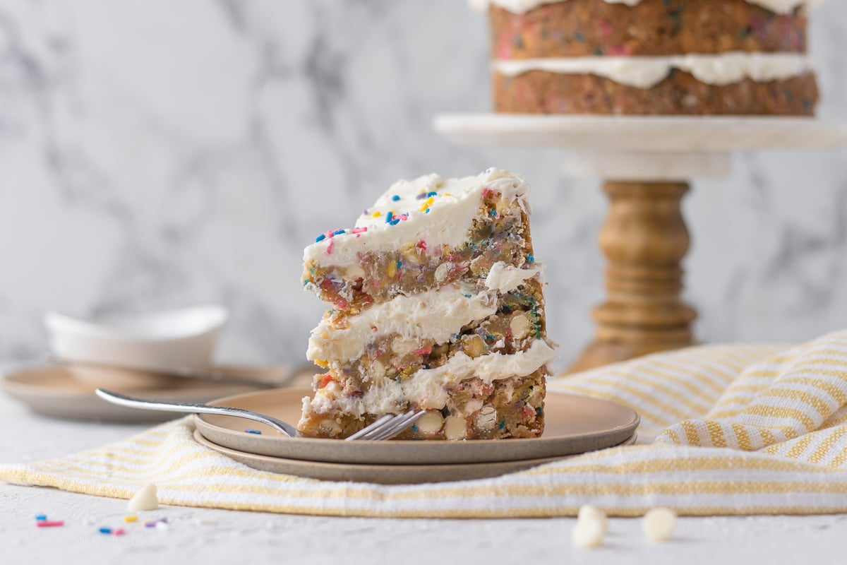 Slice of Funfetti Cookie Layer Cake with full cake in the background.