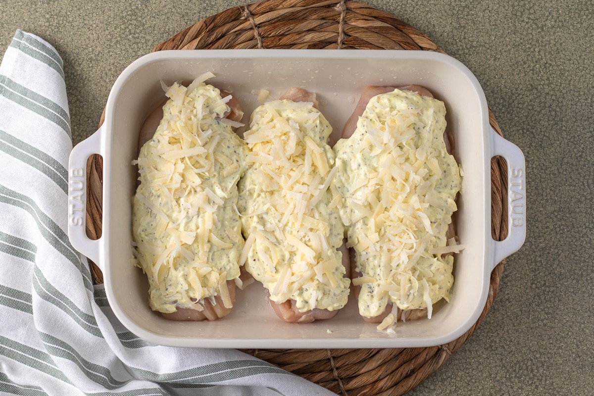 Overhead shot of chicken in baking dish with mixture and cheese on top