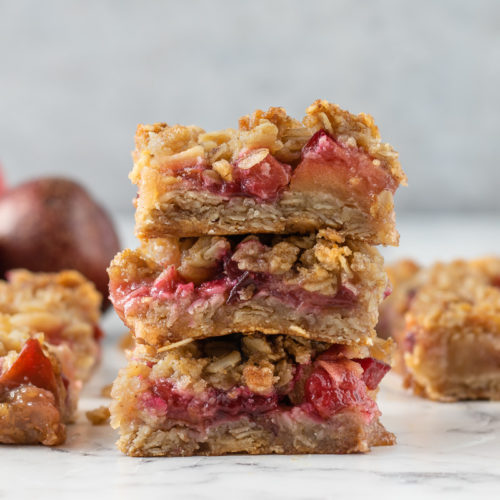 Stack of Apple and Plum Crumb bars with more in the background and plums and apples.
