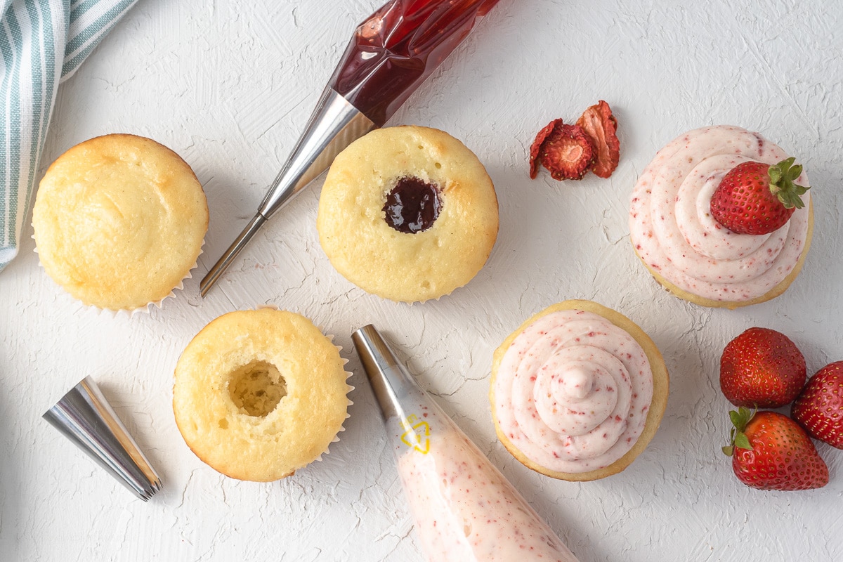 5 Steps to constructing the strawberry filled cupcakes. 1 baked vanilla cupcakes. 2 core out the center of the vanilla cupcake. 3 fill the cupcake with strawberry jam. 4 top with not so sweet strawberry buttercream. 5 topped with a fresh strawberry.