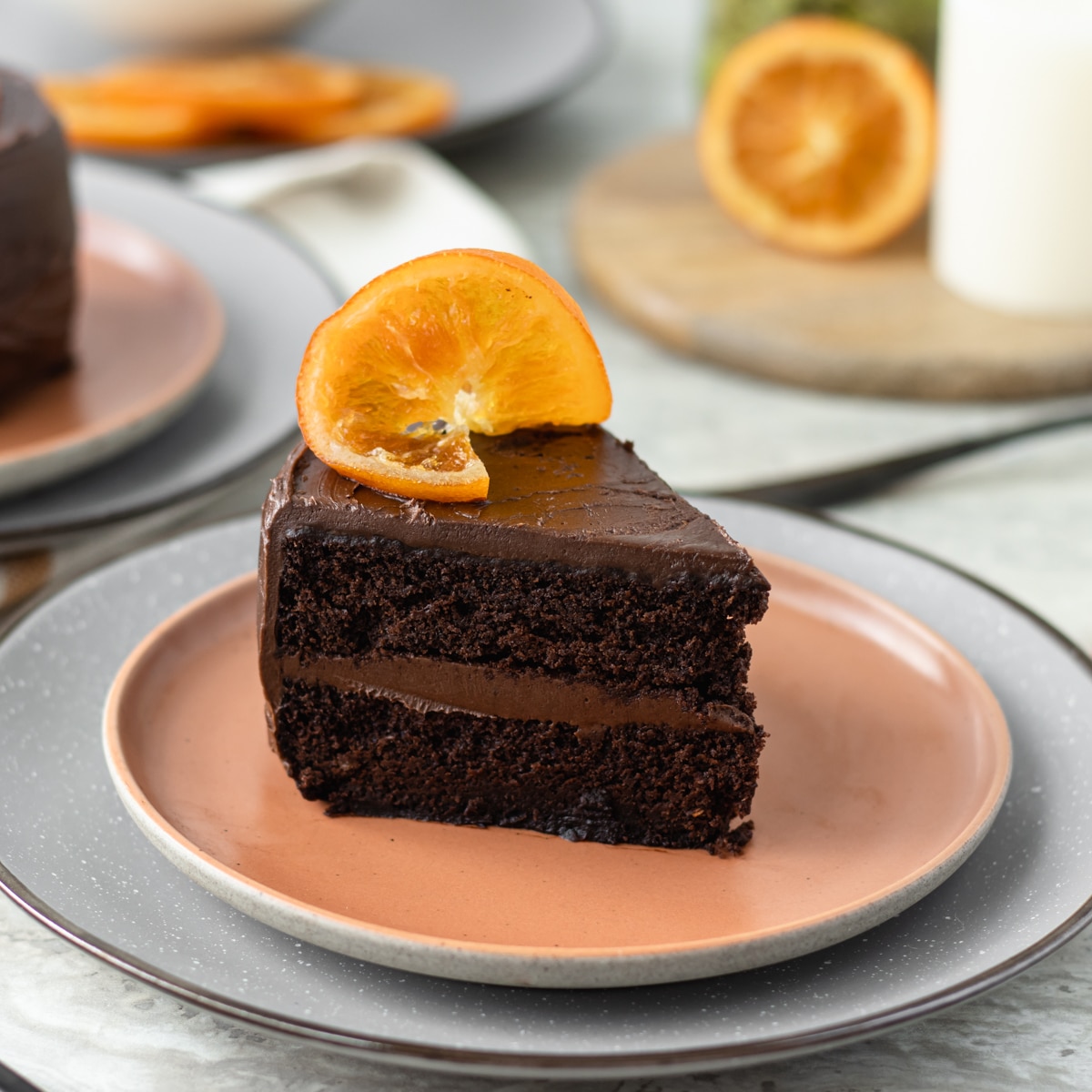Slice of Chocolate Orange Cake with another mini cake and candied orange slices in the background.