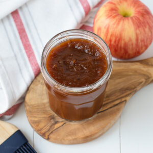 Apple Butter BBQ Sauce in a jar with a pastry brush and apple on the side.