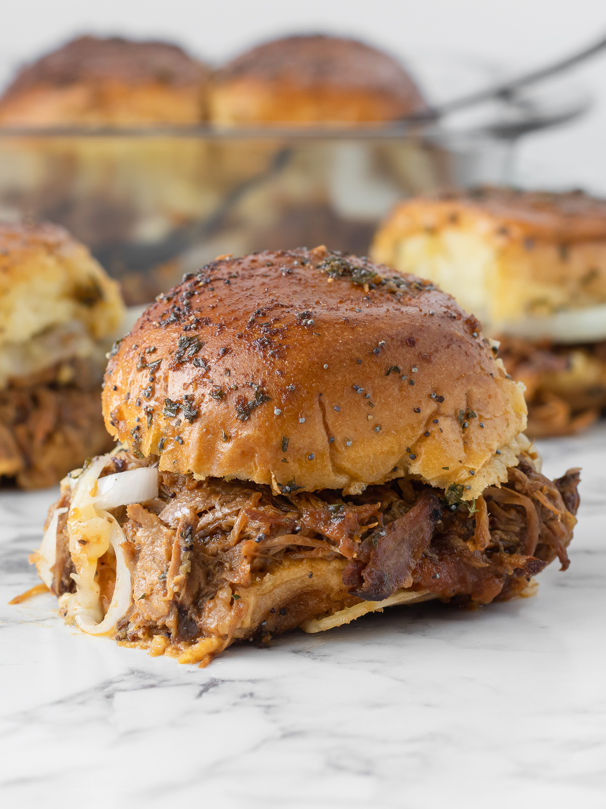 Pork sliders with toasty buns, tender apple butter bbq slow cooker pulled pork, cheese, and crunchy onions.