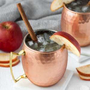 Apple Cider Mule Mocktail garnished with a cinnamon stick and slice of apple.
