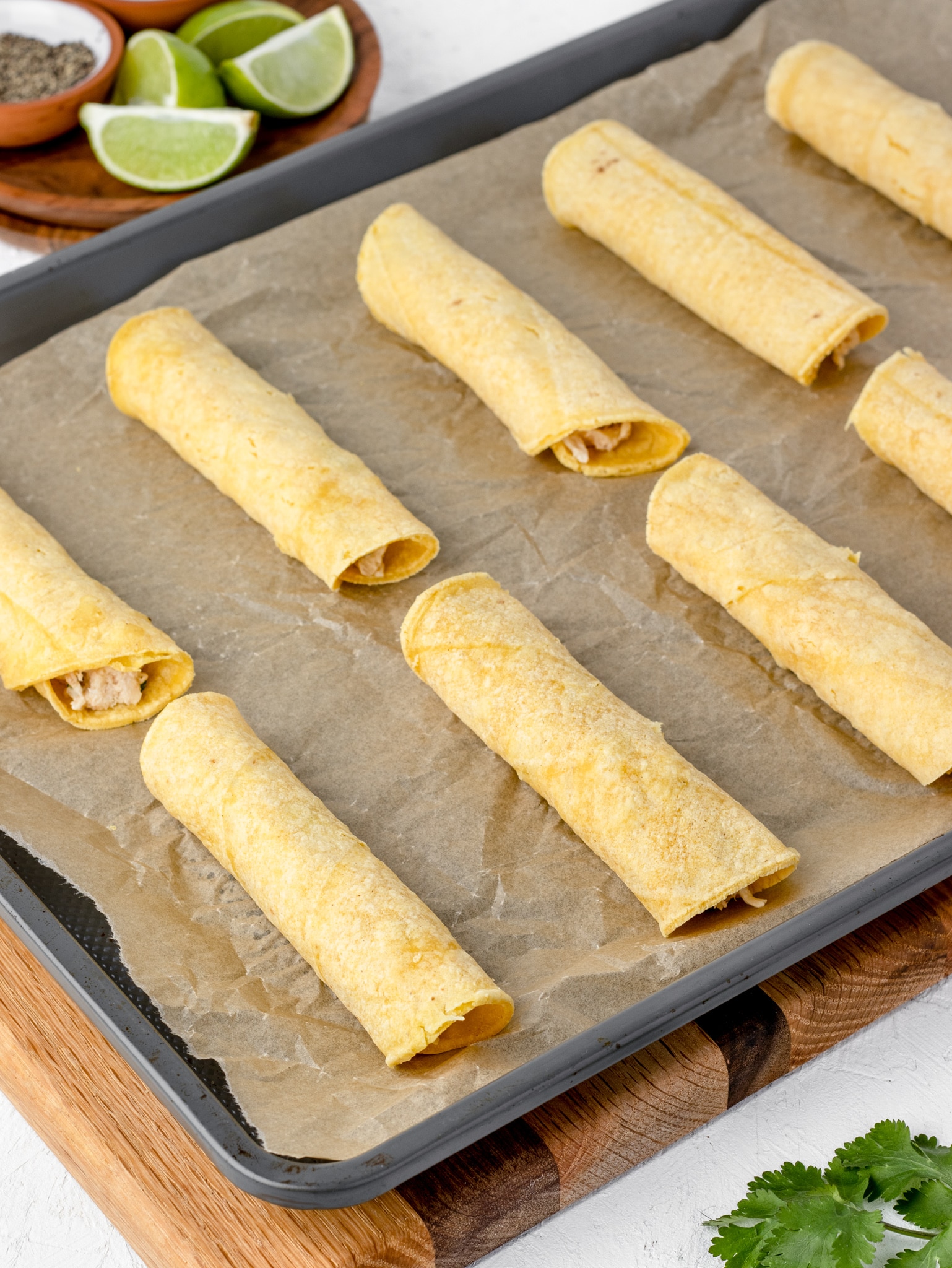 Olive oil brushed taquitos on parchment lined baking sheet ready to go in the oven.