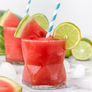 Watermelon Lime Slush in glasses with striped blue straws, lime wedges, and watermelon slices.