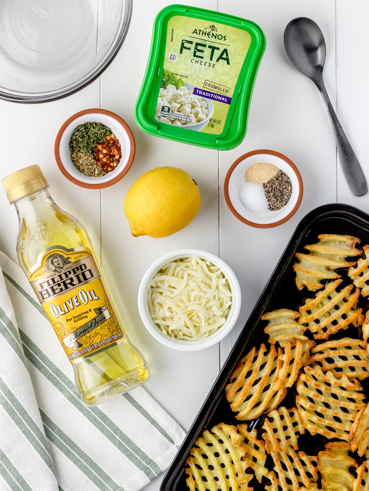 Ingredients needed are waffle fries, olive oil, lemon zest, lemon juice, red pepper flakes, oregano, parsley, garlic powder, salt and pepper, feta cheese, and mozzarella cheese.