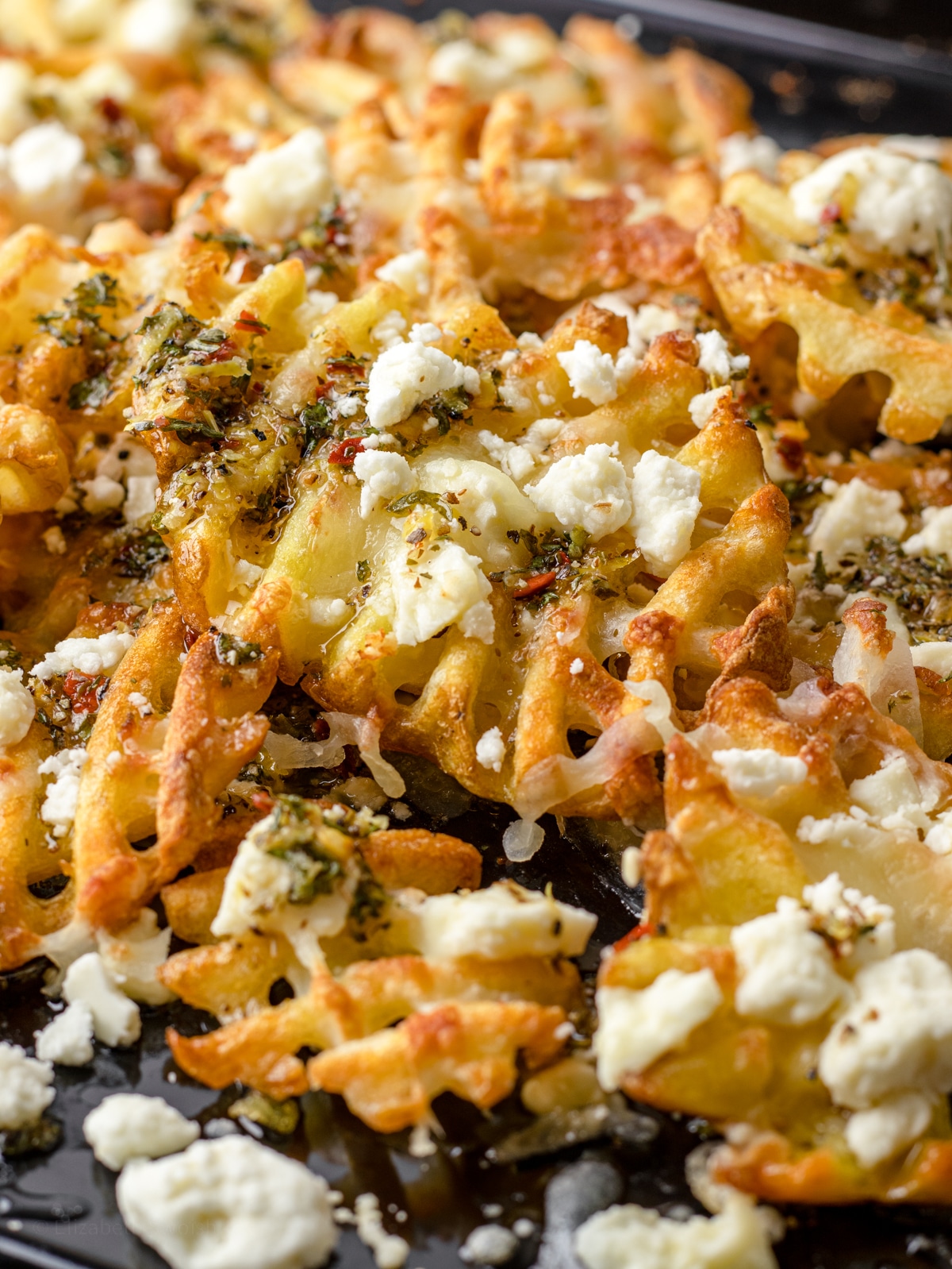 Close up of waffle fries with lemon olive oil sauce and cheeses.