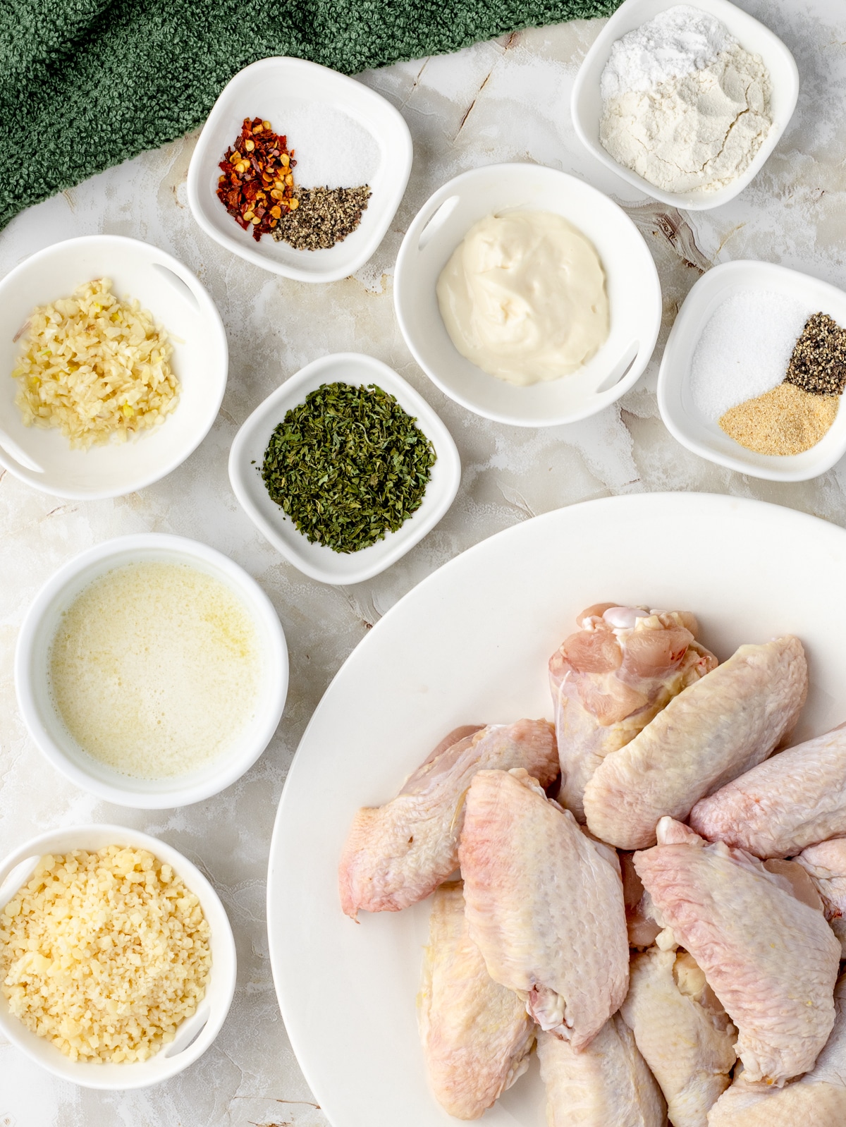 Ingredients needed for chicken wings. Chicken wings, flour, baking powder, salt, pepper, garlic powder, melted butter, mayonnaise, minced garlic, parmesan cheese, red pepper flakes, and parsley.