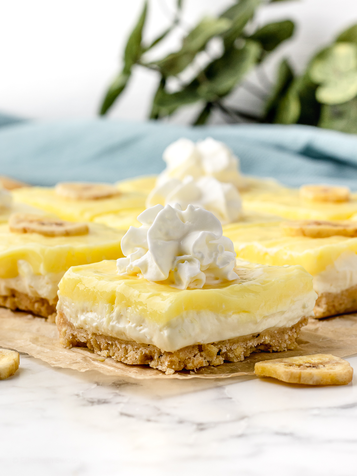 Layered Banana Pudding Cheesecake Bars cut in squares and topped with whipped cream.