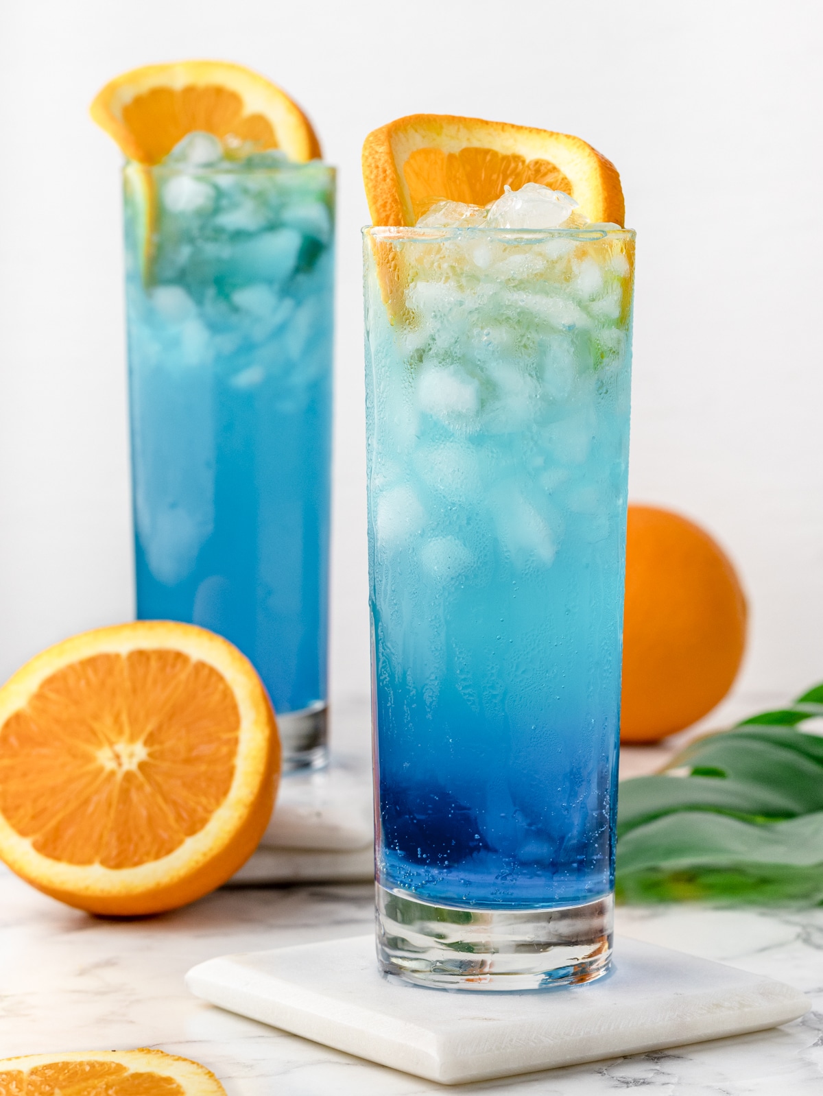 Two Blue Lagoon Mocktails garnished with a slice of orange. 