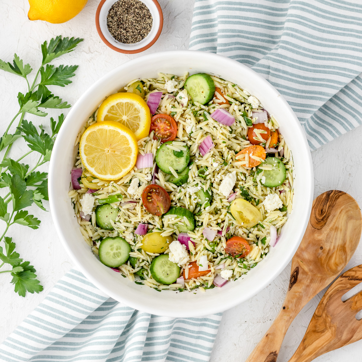 Lemon Orzo Salad toppings mixed in with dressing made of lemon juice, zest, olive oil, salt and pepper.