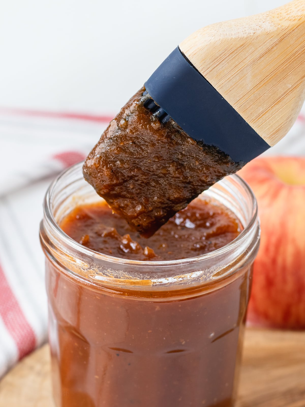 Apple Butter BBQ Sauce in a jar being scooped out with a silicone pastry brush.