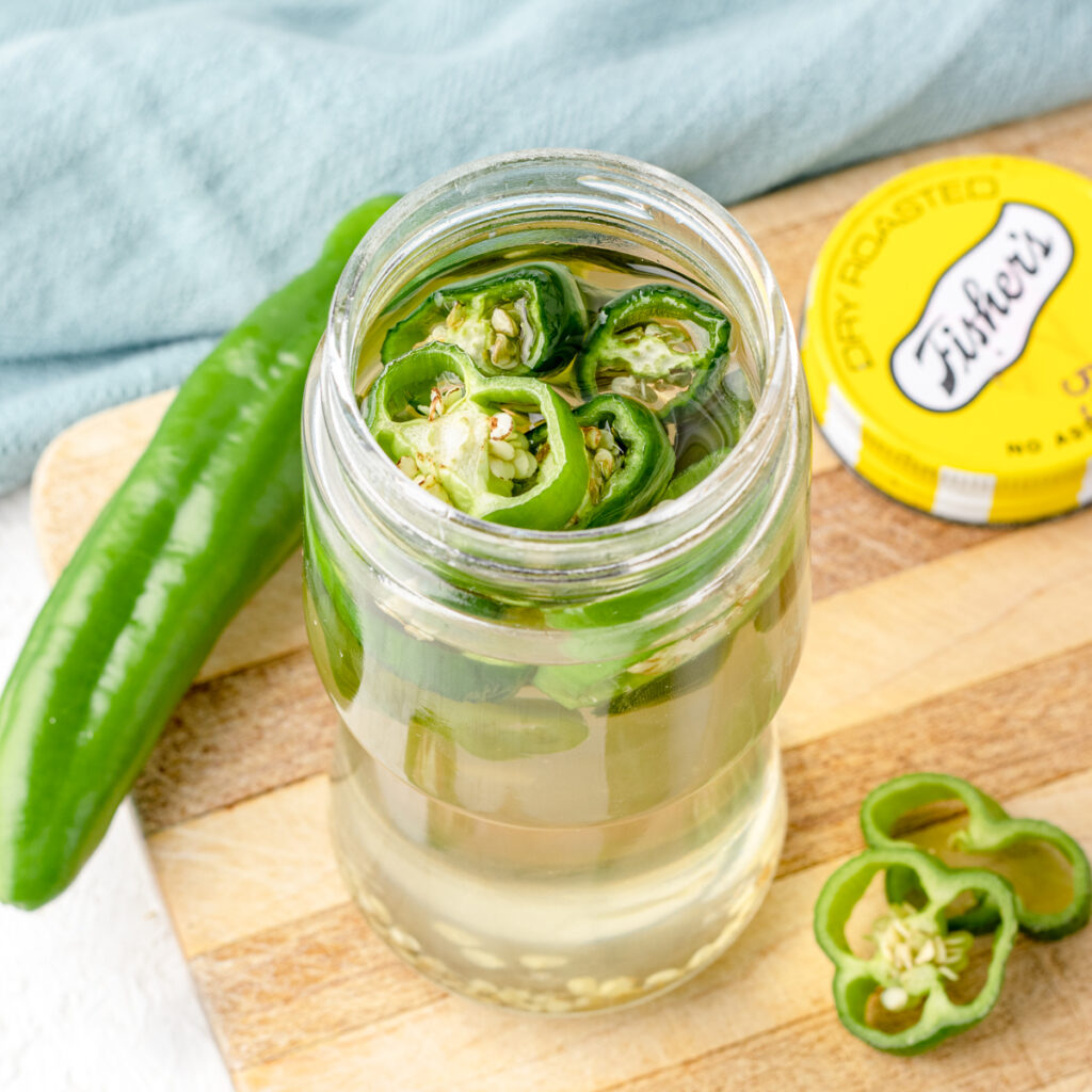 Jalapeno Simple Syrup in a jar with the lid removed and surrounded by jalapenos and slices.