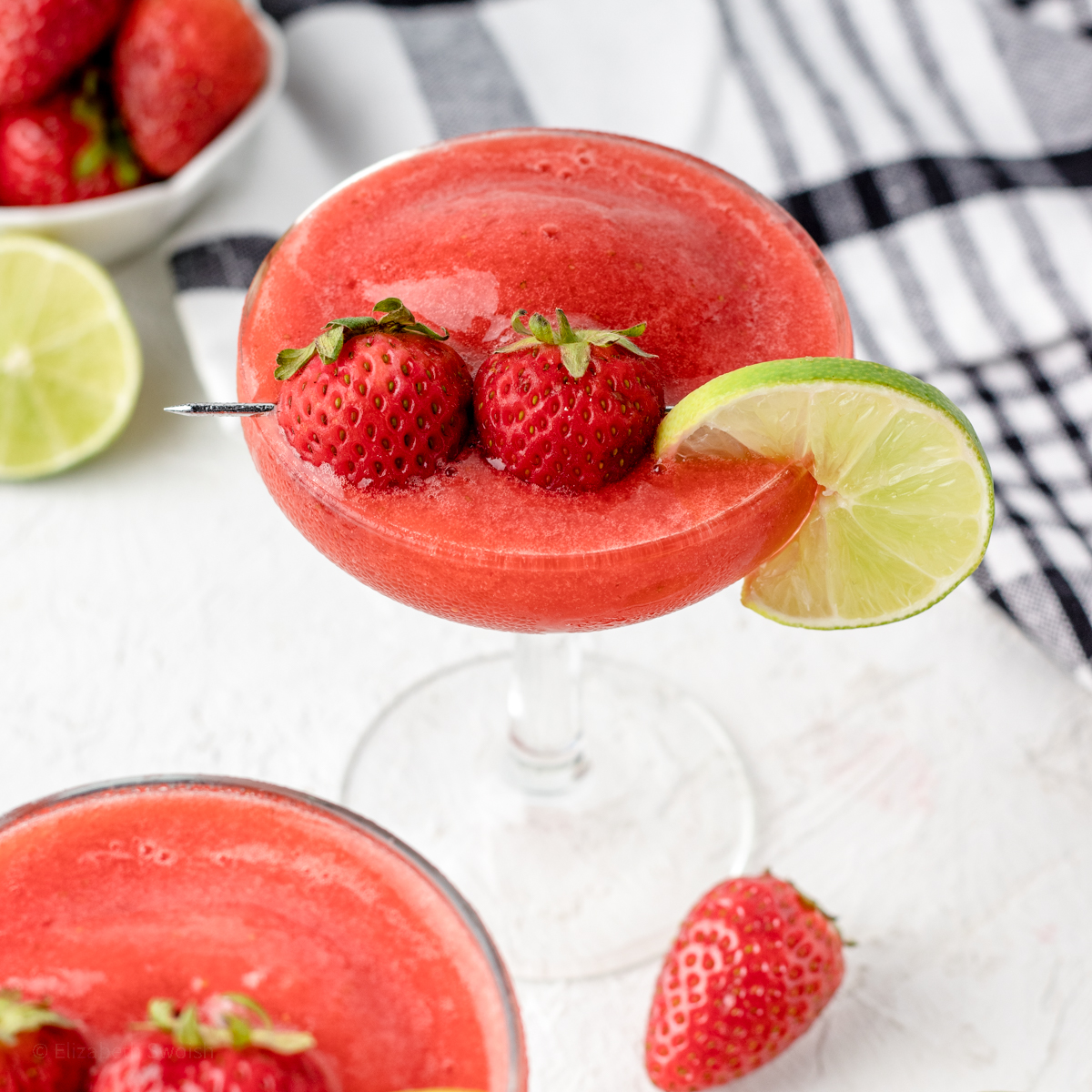 Two Strawberry Daiquiri Mocktails in stemmed glasses, garnished with a lime slice and two small strawberries.