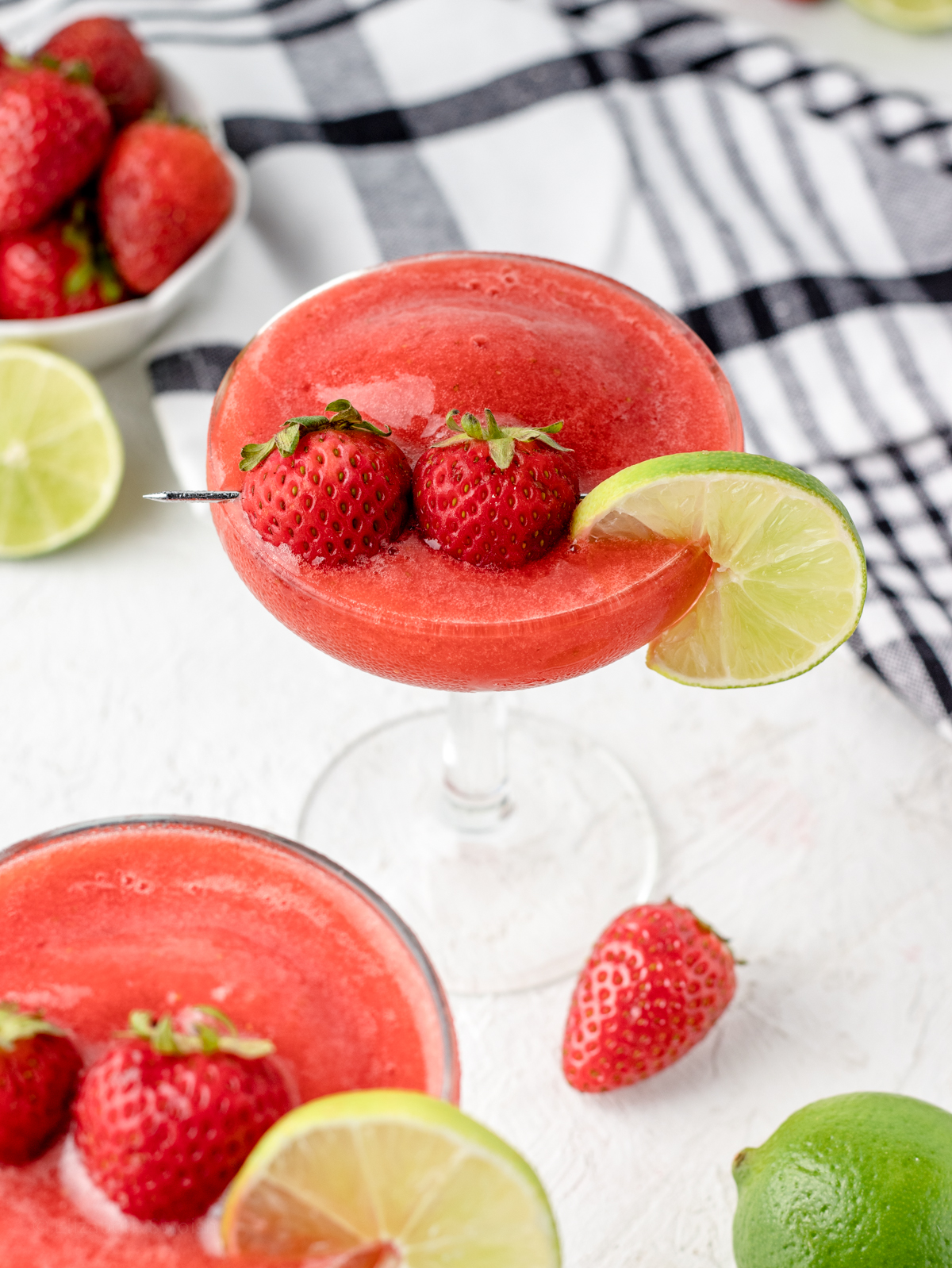 Two Strawberry Daiquiri Mocktails in stemmed glasses, garnished with a lime slice and two small strawberries.