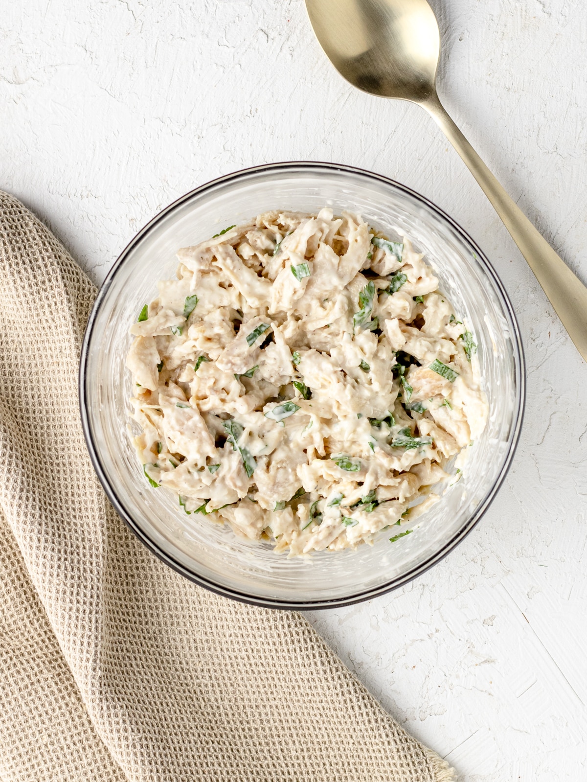 Shredded chicken mixed together in a bowl with ranch dressing and fresh parsley.
