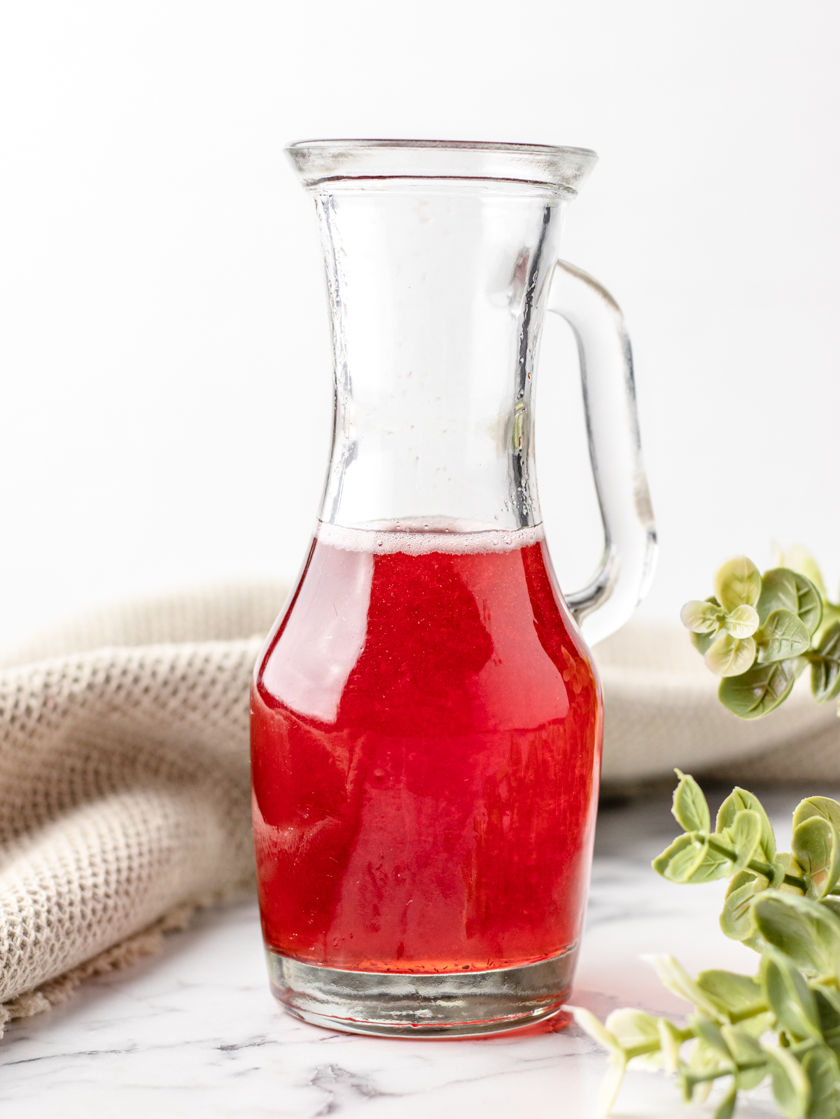 Strawberry Simple Syrup using discarded strawberry tops in a glass handled container.
