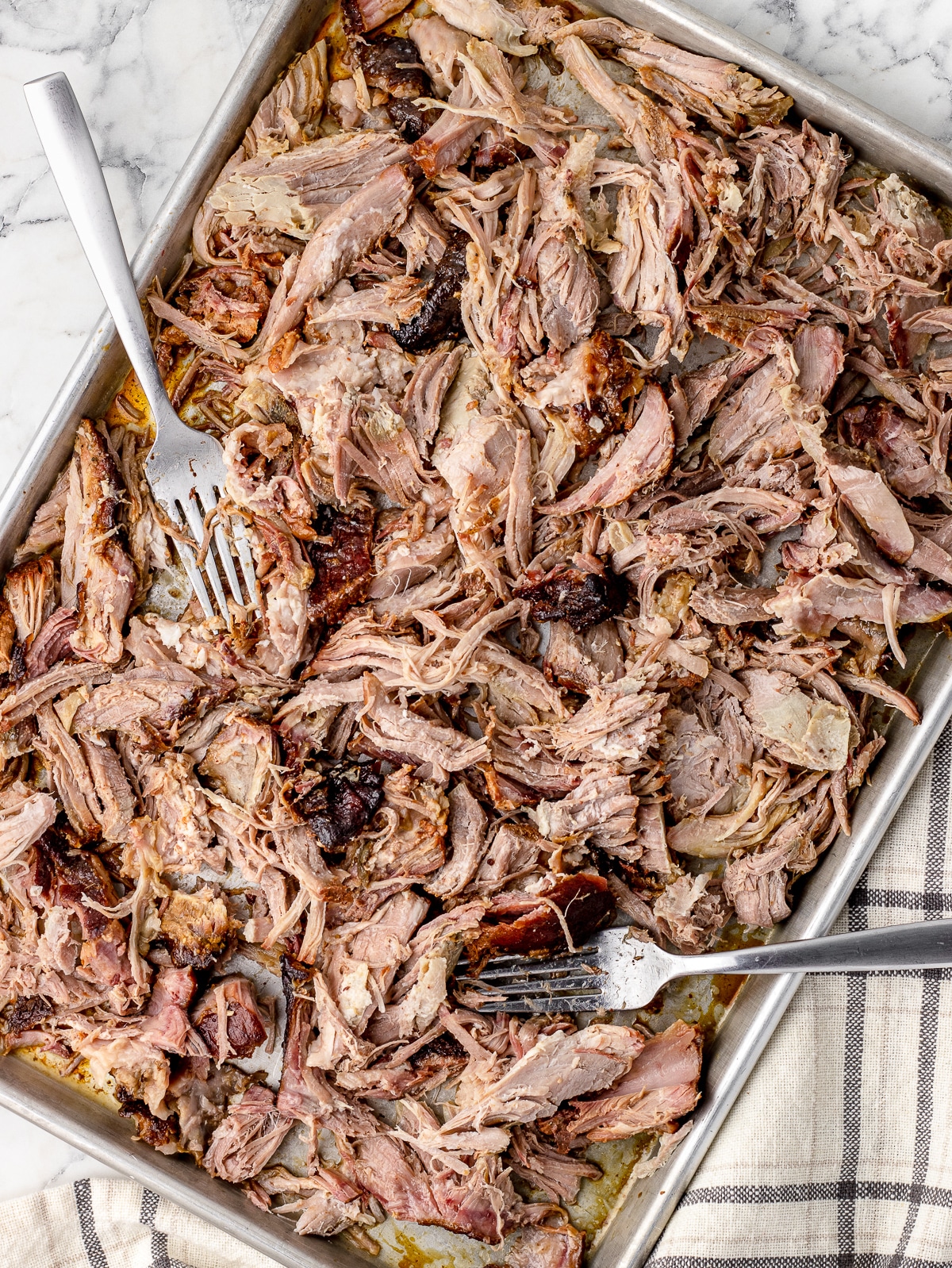 Shredded smoked pulled pork on a tray with two forks.