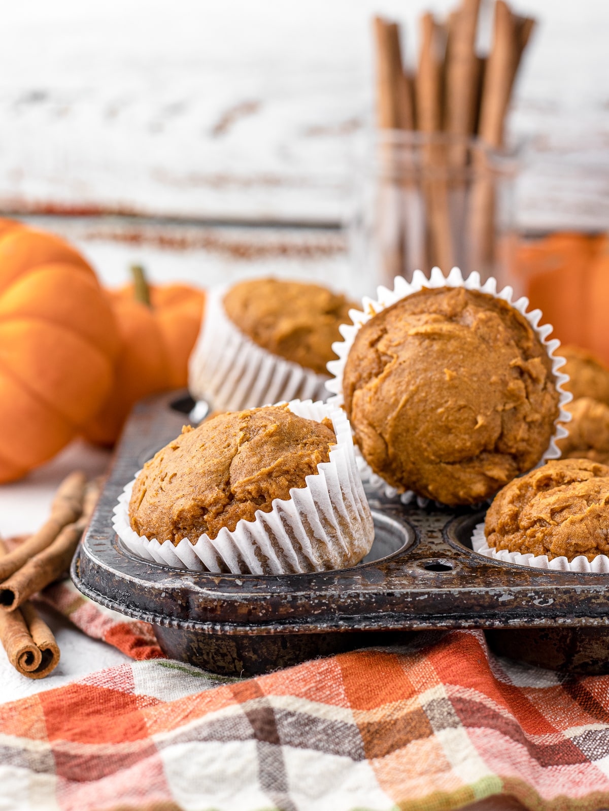 3 ingredient pumpkin muffins in an antique pan surrounded by mini pumpkins, and cinnamon sticks.
