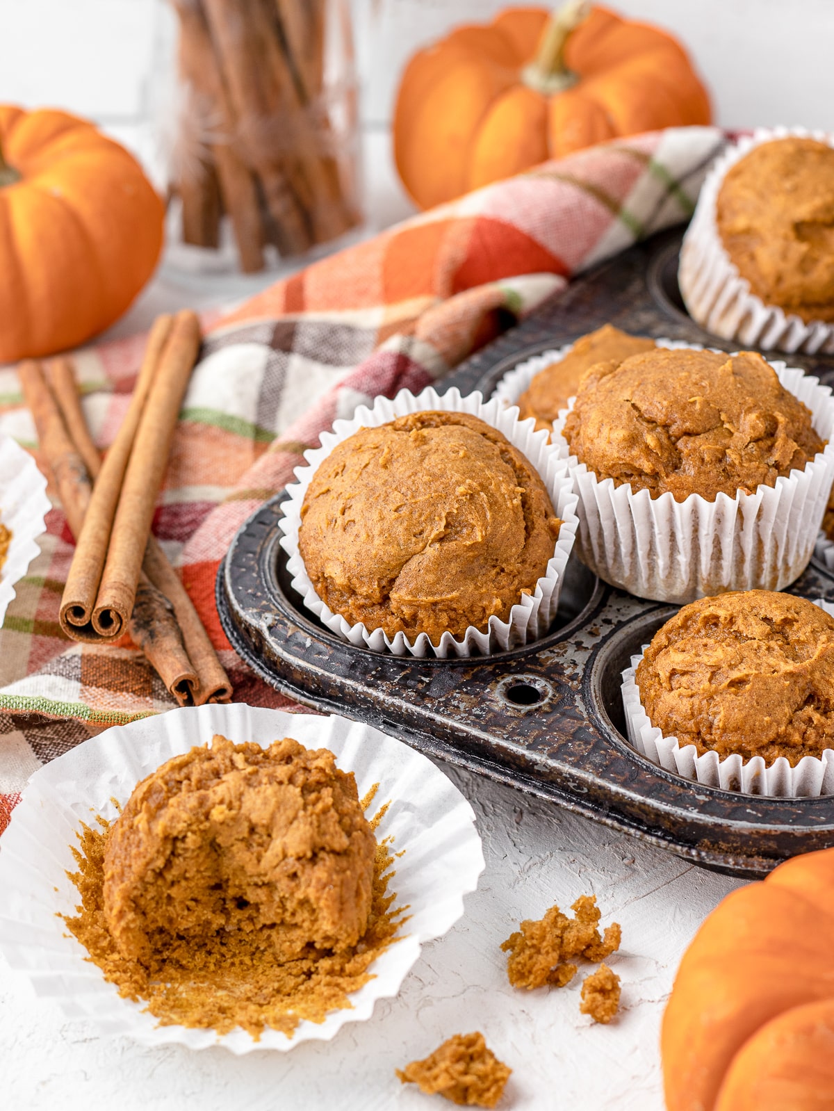 Pumpkin muffins surrounded by mini pumpkins, cinnamon sticks, and half eaten muffins.