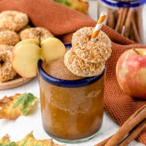 Creamy and delicious Apple Cider Slushie surrounded by mini donuts, apples, and fall festive leaves.