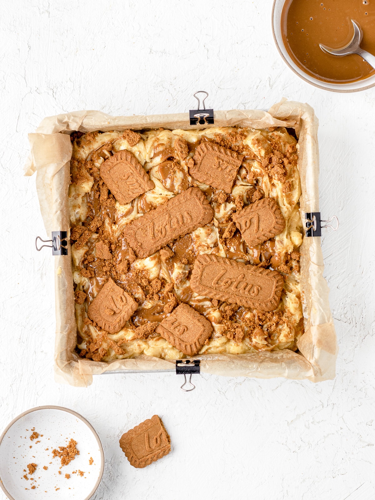 In a baking pan, the blondie batter with swirls of Biscoff cookie butter and crumbled Biscoff cookies.