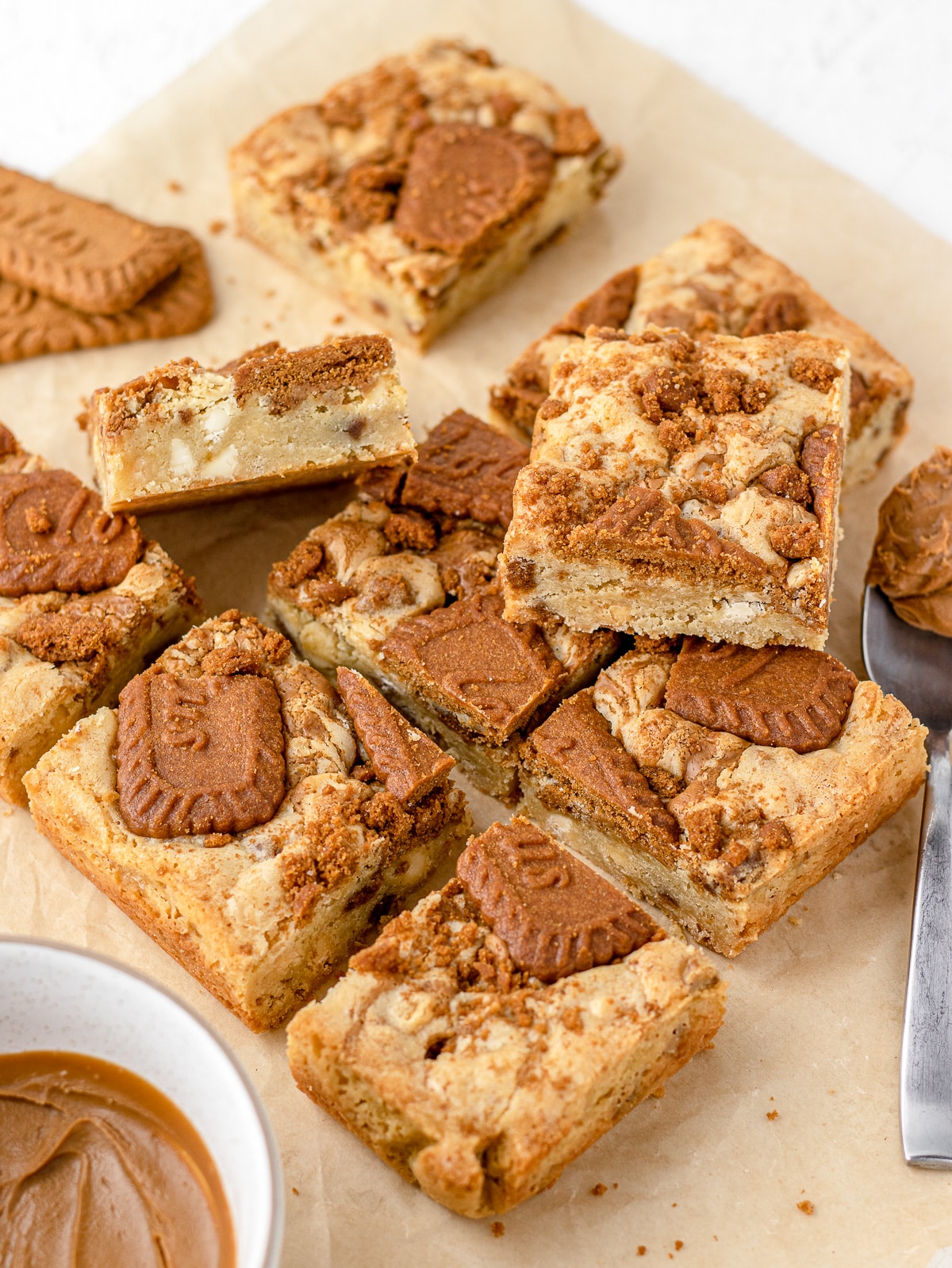 Blondies arranged on top of parchment paper with Biscoff cookie butter on the side.