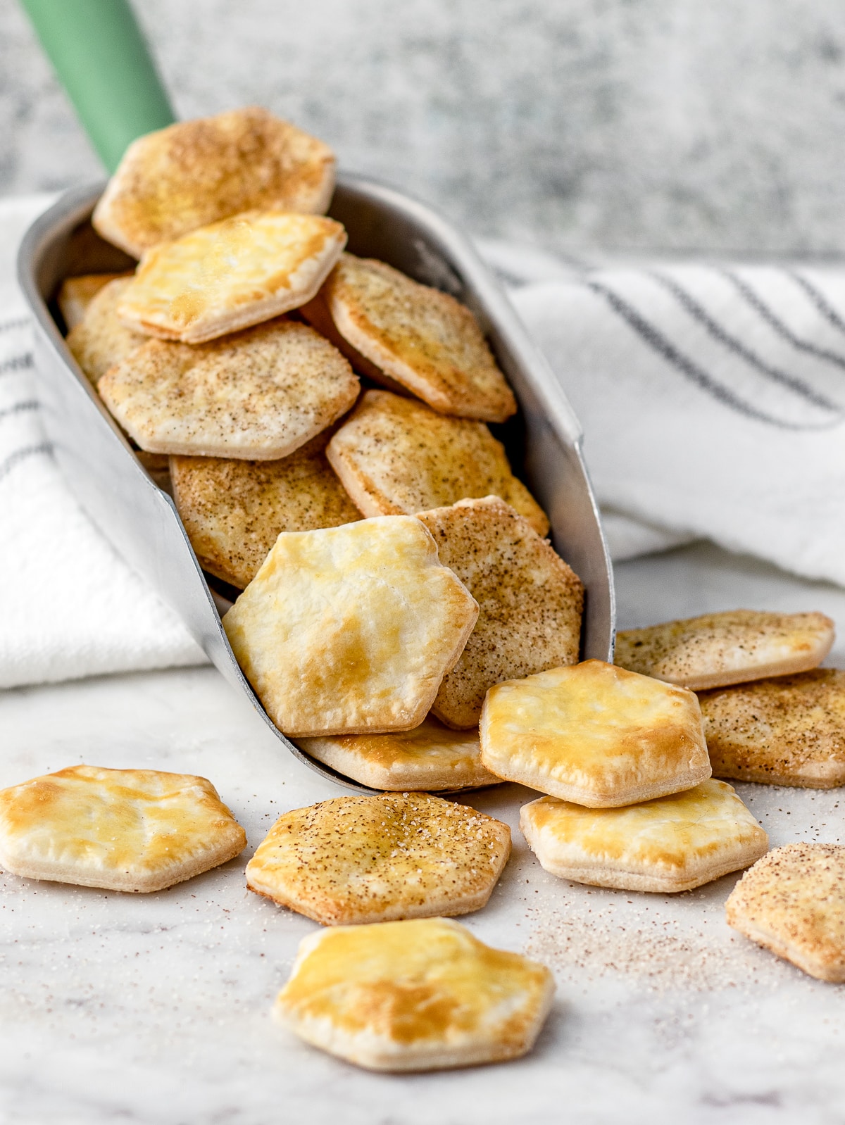 Pie crust cookies falling out of a scoop. A variety of cinnamon sugar and plain chips is pictured.