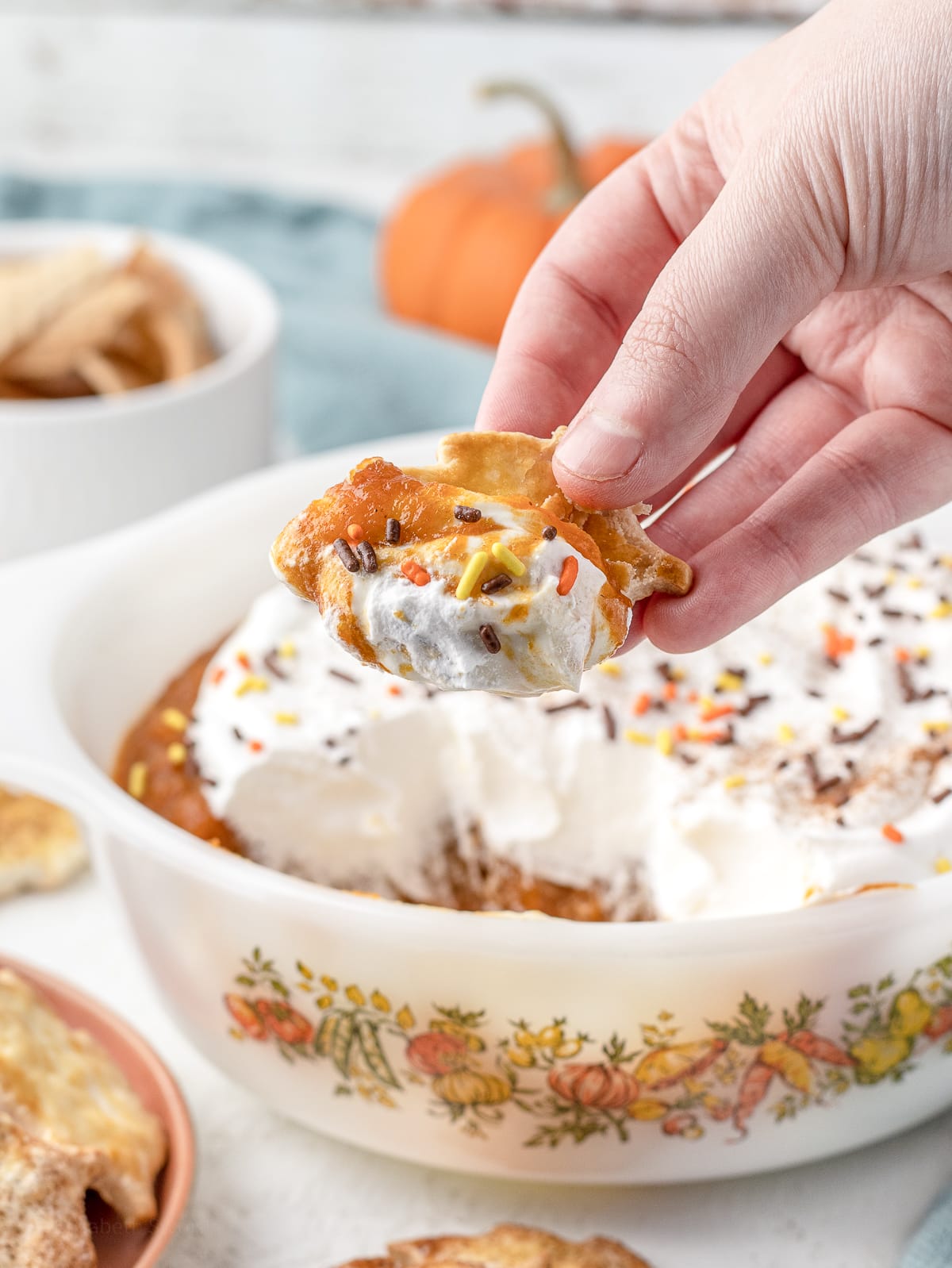 Hand holding a pie crust chip with a large scoop of Pumpkin Pie Dip.