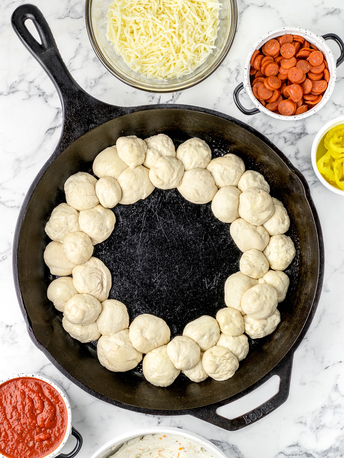 Rolled pizza dough balls lined around the perimeter of a greased cast iron skillet.