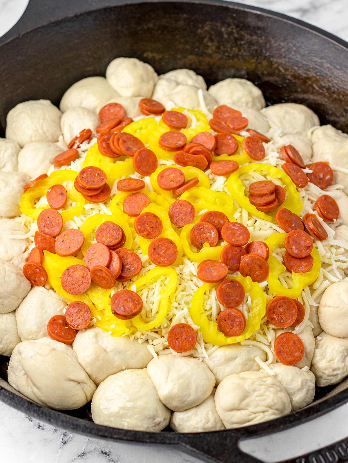 Cast iron with pizza dough balls and layer one of dip, pizza sauce, mozzarella cheese, mini pepperonis, and pepperoncinis.