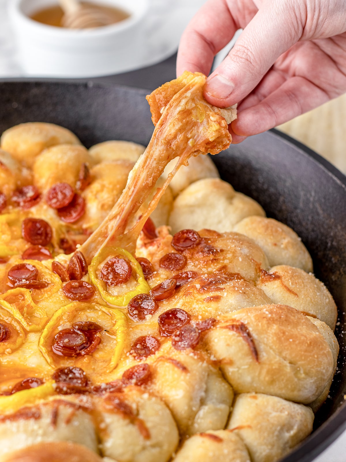 A hand pulling a pizza dough ball from the cheesy pizza dip.