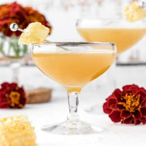 Apple Bee's Knees Mocktail in coupe glass garnished with honeycomb and red marigolds.