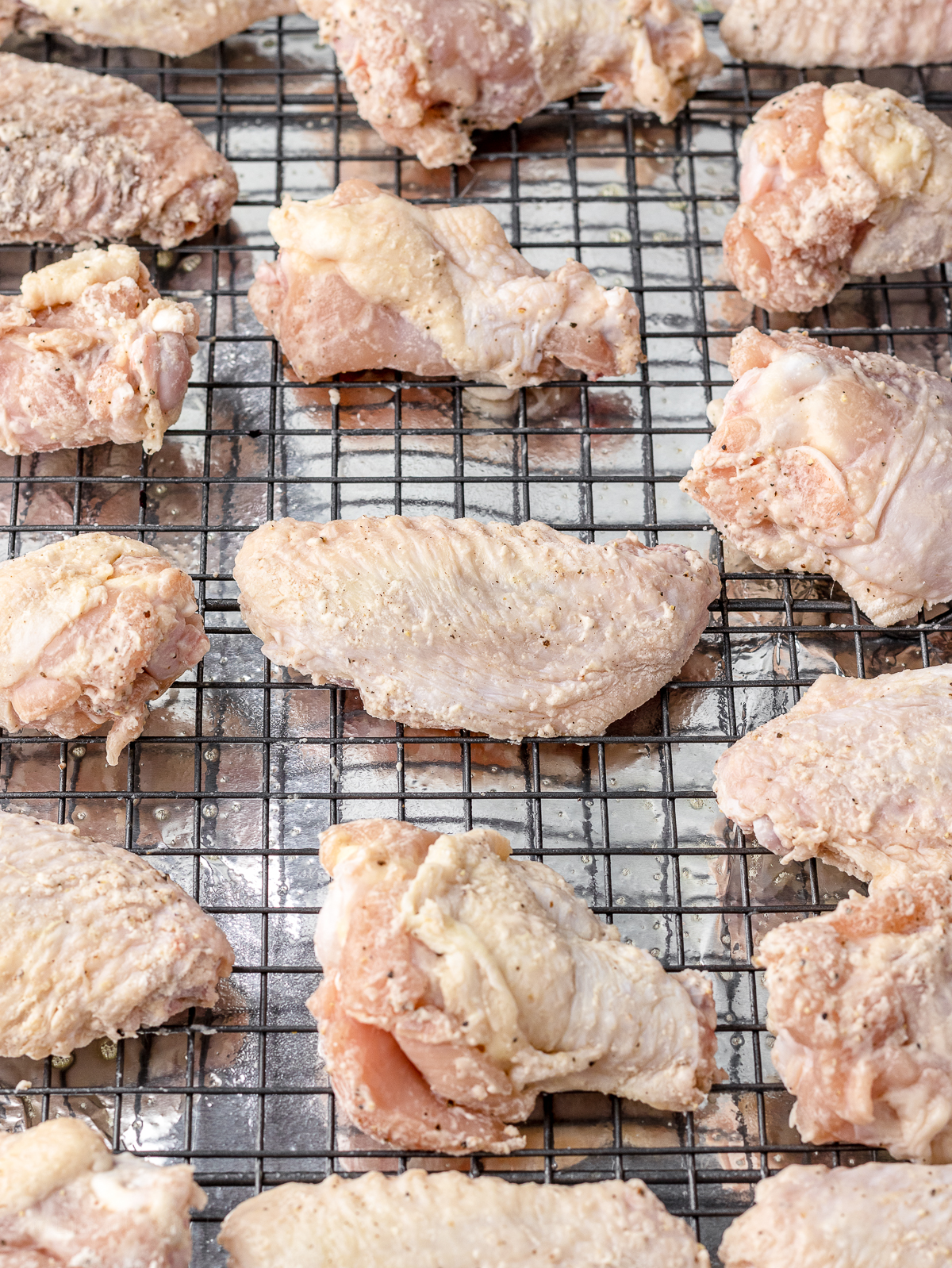 Chicken wings tossed in seasoning and baking powder on a rack lined baking sheet. Ready to go in the oven.