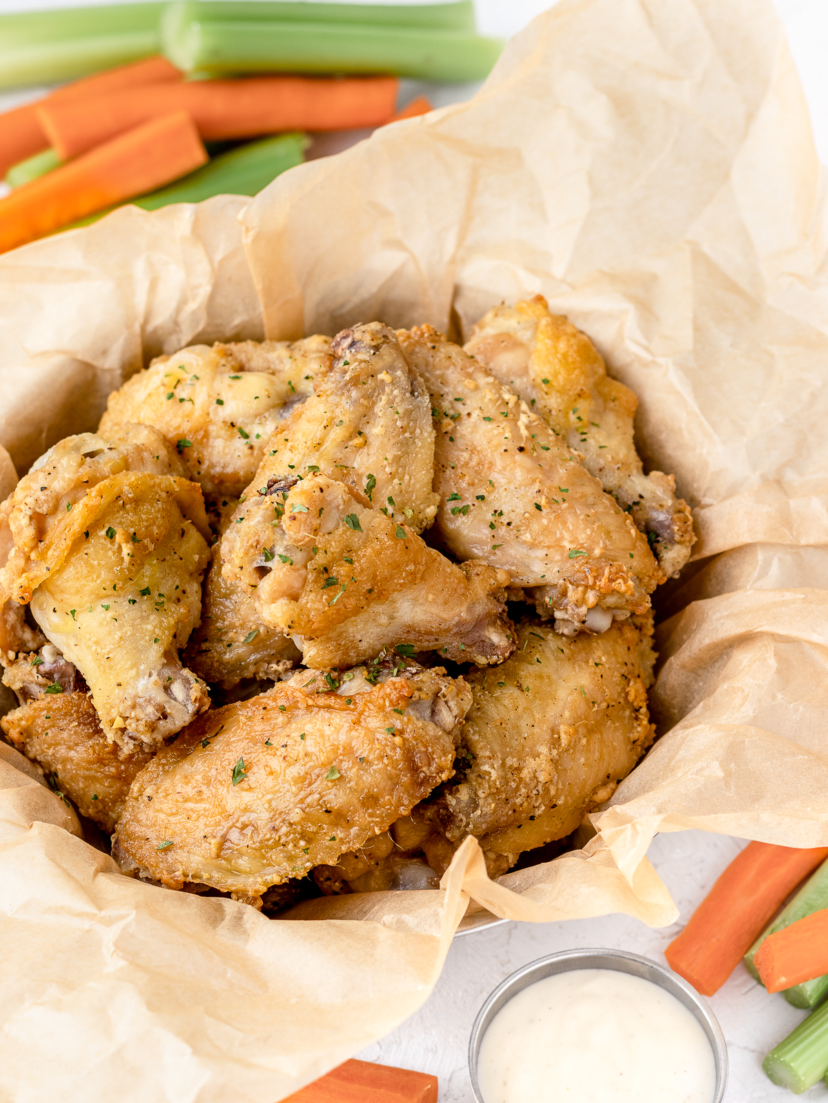 Oven Baked Chicken wings in a parchment lined basket. Surrounded by carrots, celery, and dipping sauce.