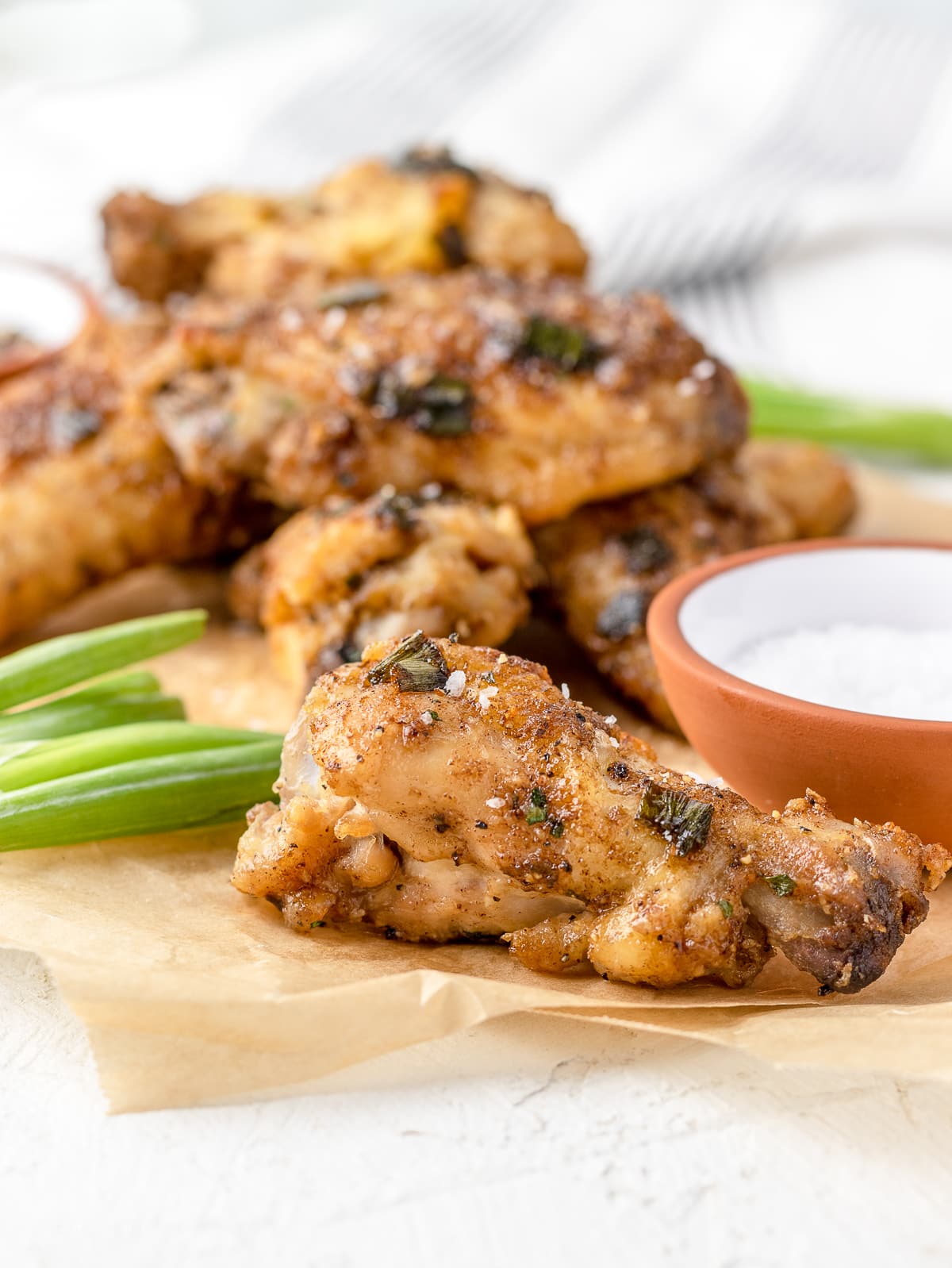 Close up of Salt and Pepper Wing garnished with scallions, flaky salt, and cracked black peppercorns.
