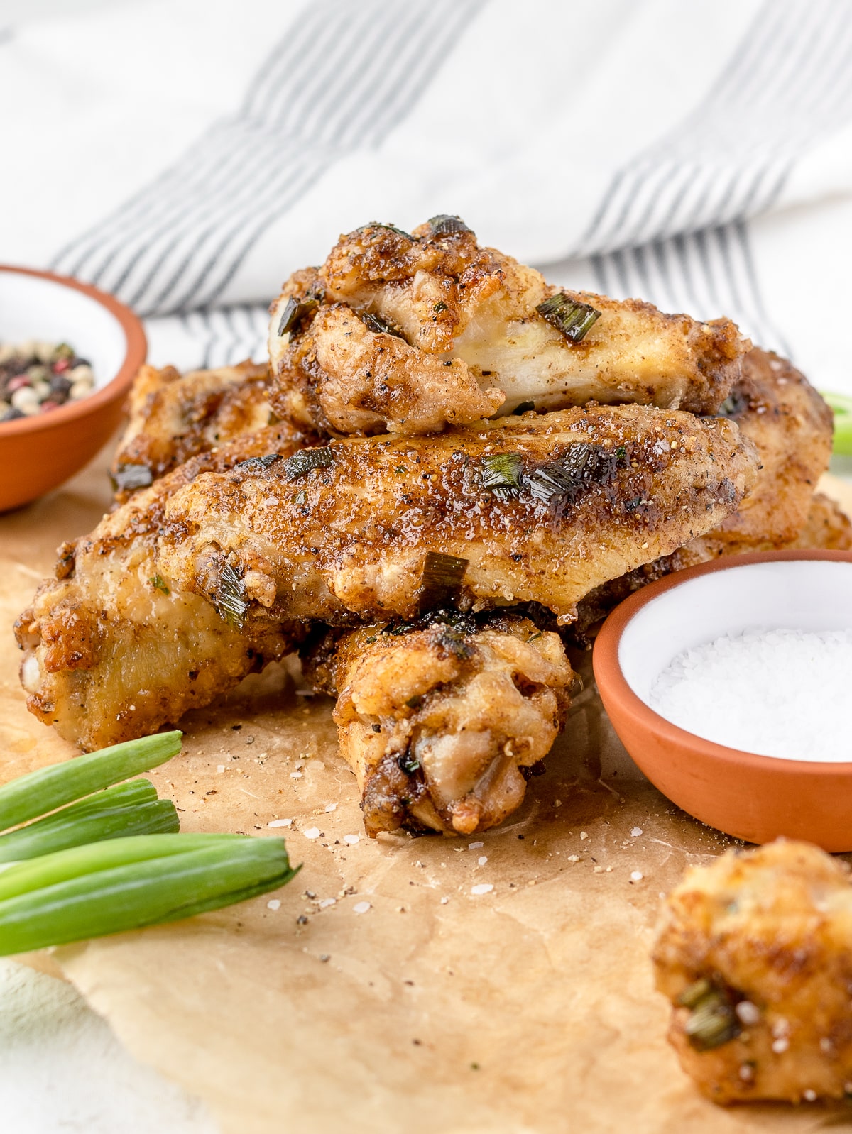 Salt and Pepper Wings stacked up and ready to eat surrounded by extra salt, pepper, and scallions.